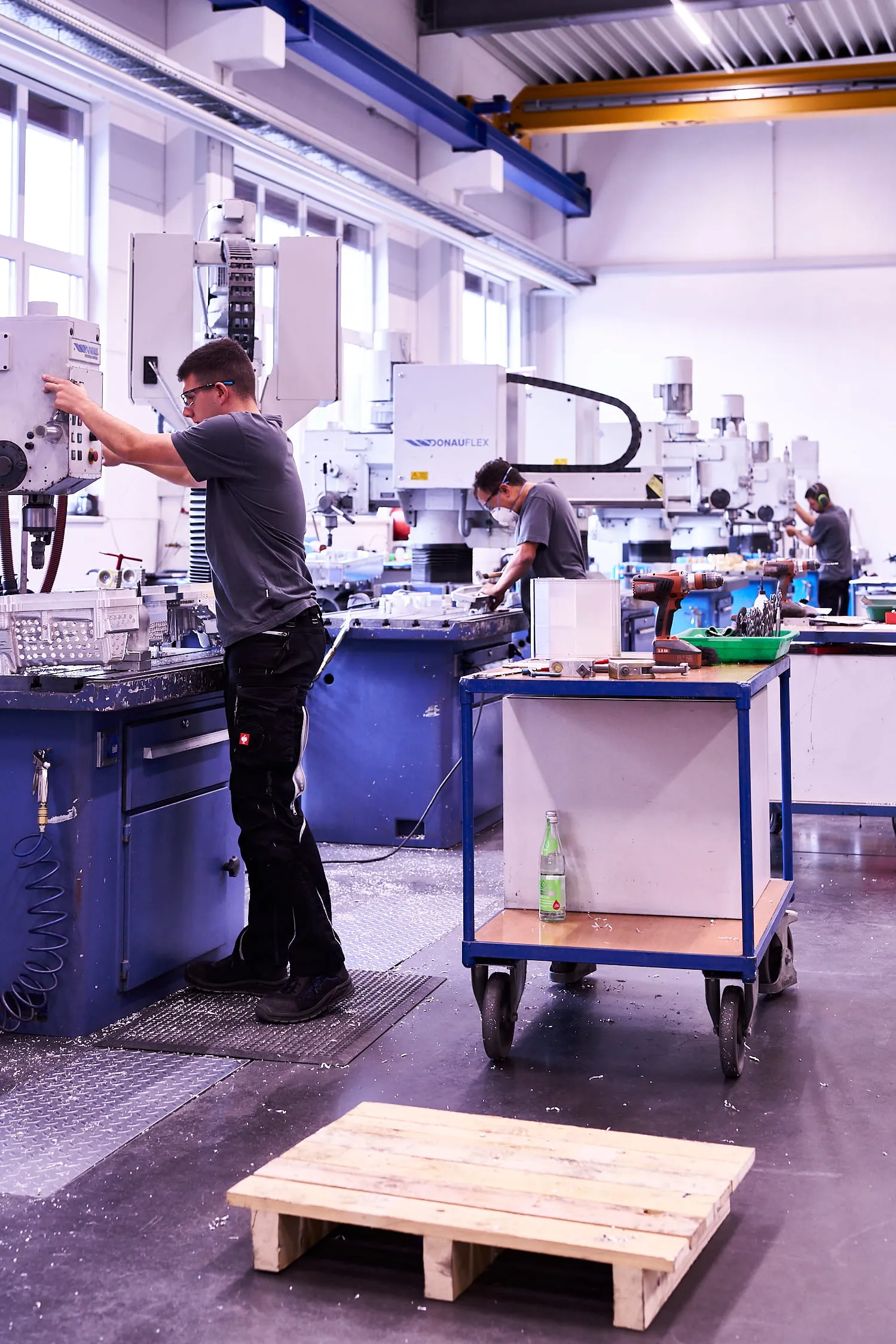 Mitarbeiter richtet eine Fräsmaschine ein, dahinter weitere Kollegen an den Maschinen der Halle