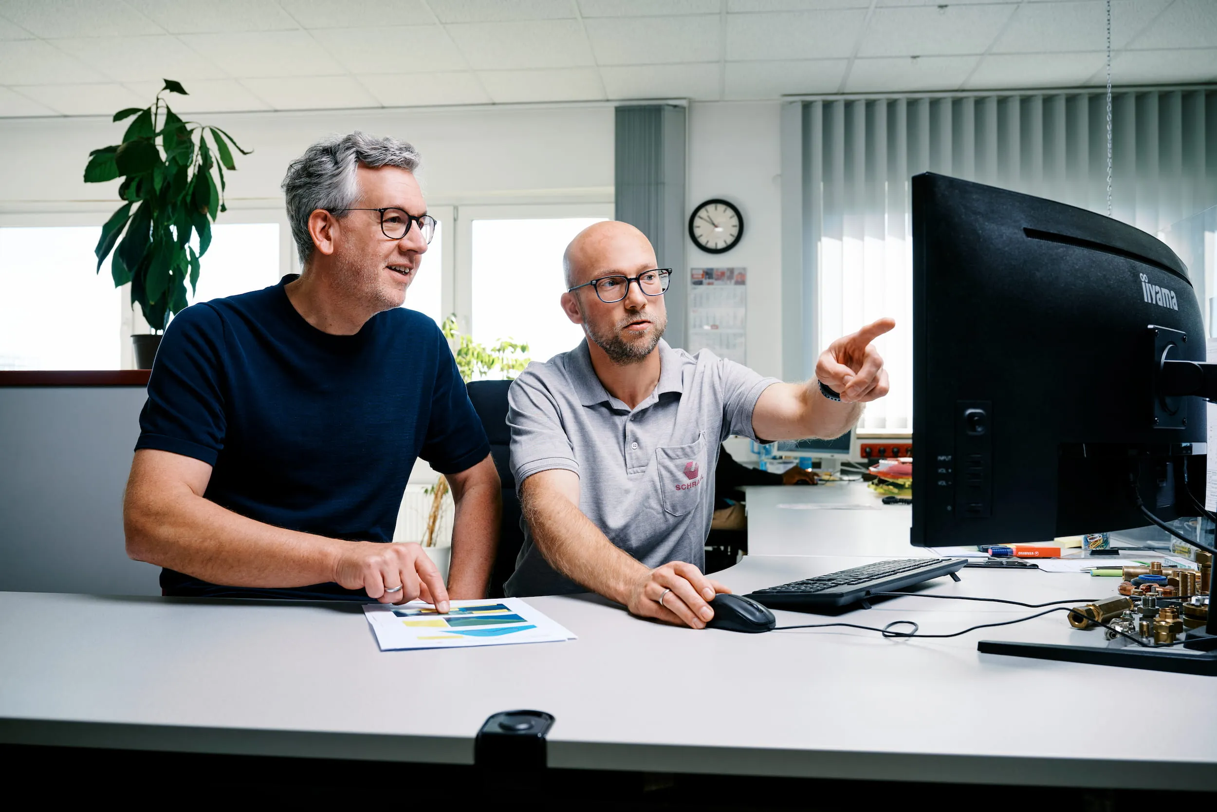 Konstrukteur bespricht mit seinem Chef am Schreibtisch eine Konstruktion und zeigt dabei auf den Bildschirm