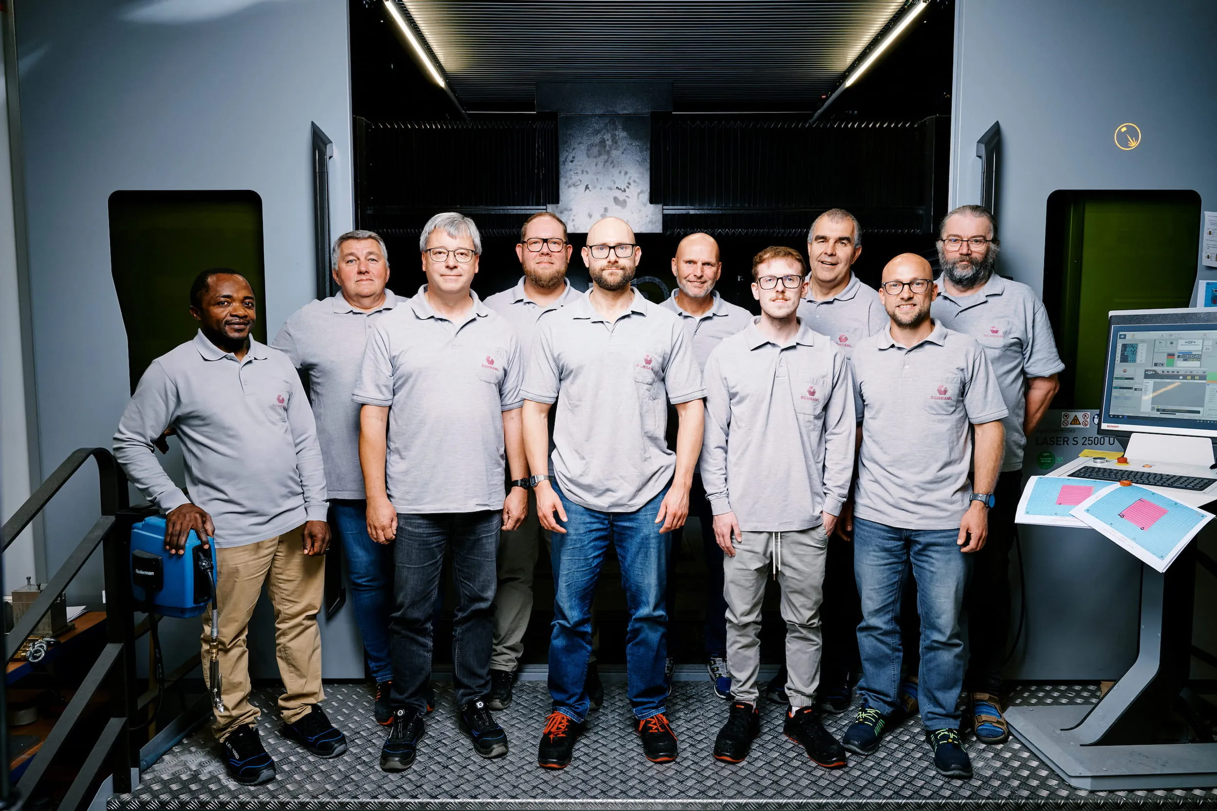 Das Konstruktionsteam von SCHRAML in grauen Poloshirts vor der geöffneten Laseranlage in der Halle